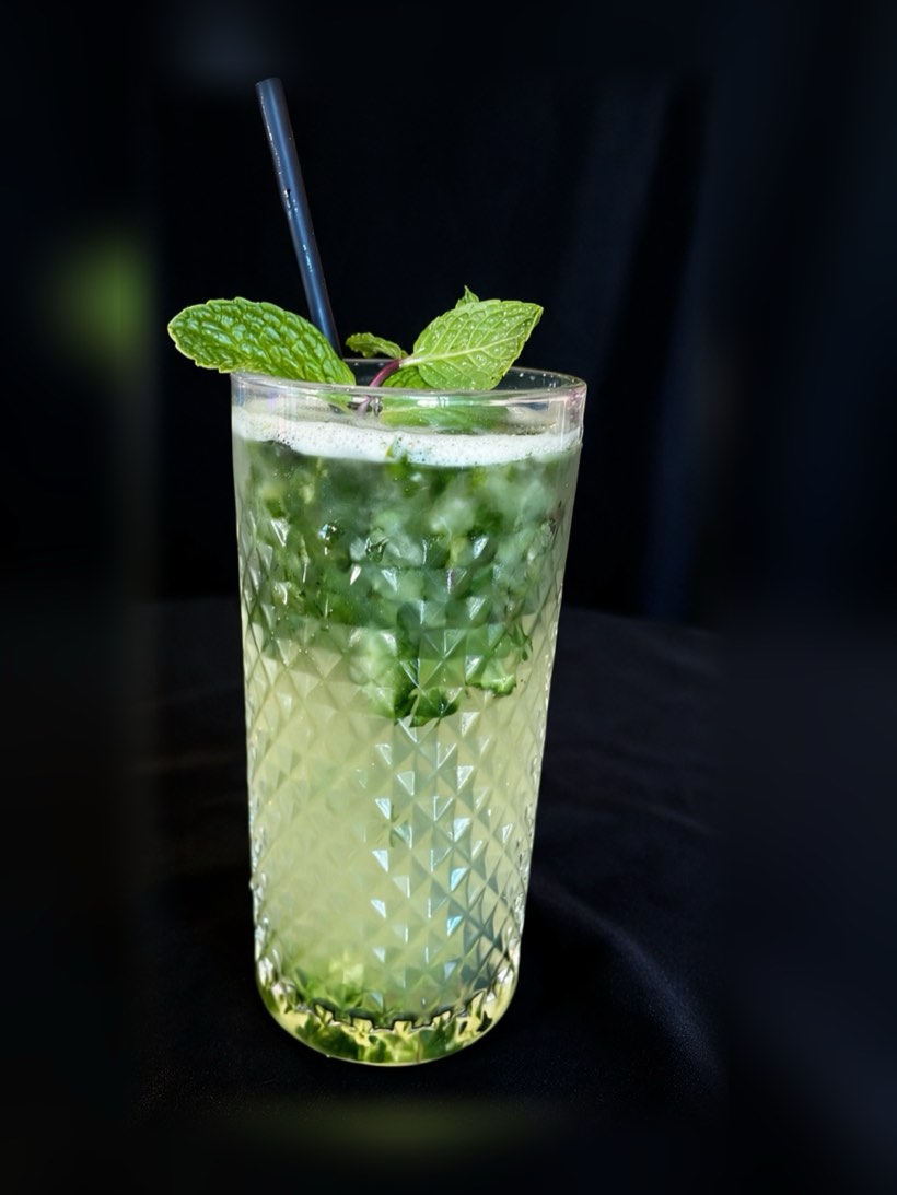 Tall faceted glass of pale green cucumber mojito over crushed mint with a mint sprig