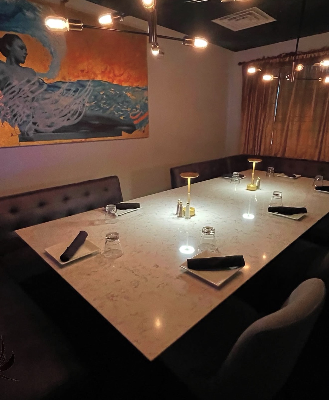 The Chef’s Room: a marble table set for six under warm edison lighting, tufted banquettes and a large mural
