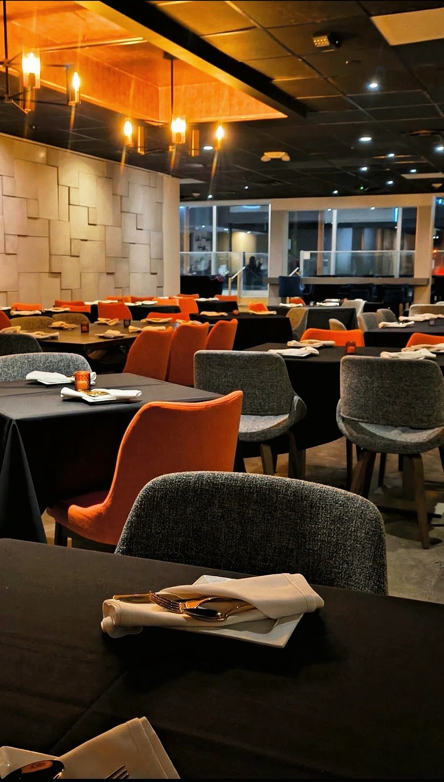 The Saffron dining room set for service, with orange and grey chairs at black-linen tables under brass chandeliers