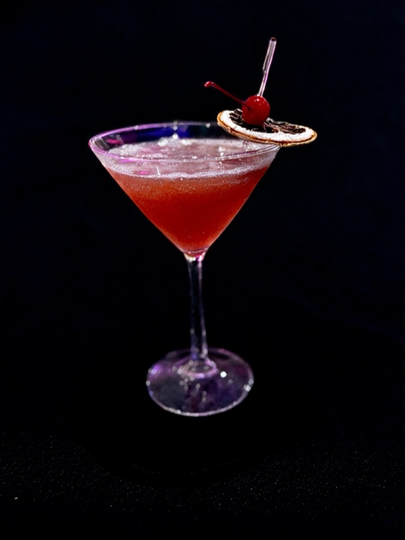 Deep red martini with a maraschino cherry and a dried citrus wheel on the rim